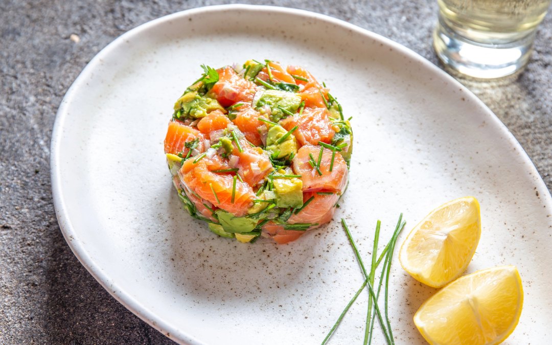 PERUVIAN FOOD. Salmon ceviche with avocado, spring onion and lemon on white plate served with white wine