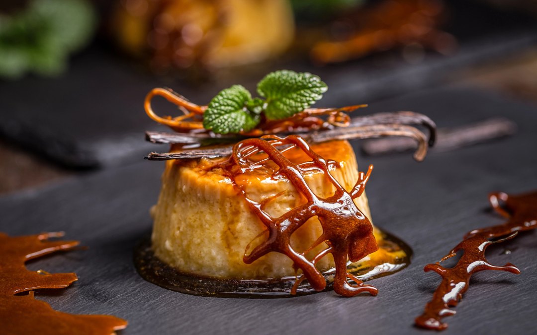 Flan, a typical Latin American dessert, served on a dark wooden table, decorated with caramel, mint leaves, and a stick of vanilla