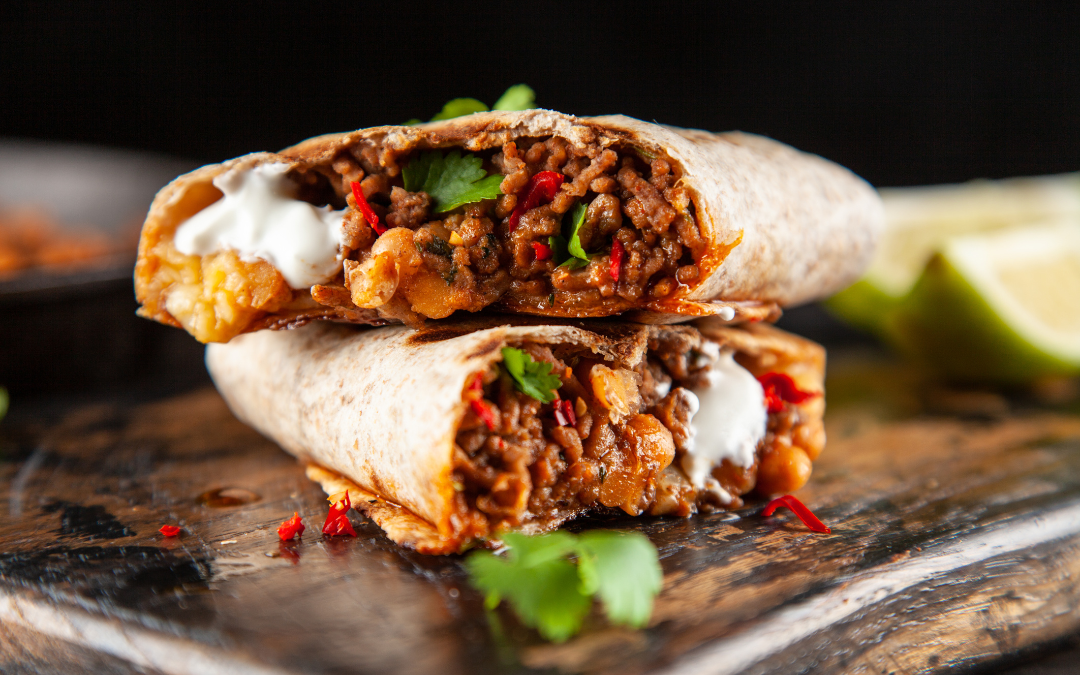 close up of a steak burrito cut in half and stacked on a wooden board